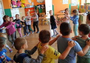 Dzieci tańczą. Trzymając się za ramiona tworzą korowód wokół sali.